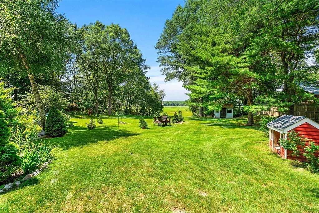 Expansive lawn with mature plantings, playhouse, and marsh beyond